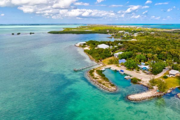Aerial view of a turquoise harbor with a small marina, rocky shoreline, and dense tropical greenery along a coastal village.