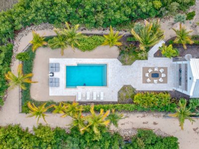 Aerial view of a rectangular pool surrounded by a stone patio, lounge chairs, and a dining area amid palm trees and tropical vegetation.
